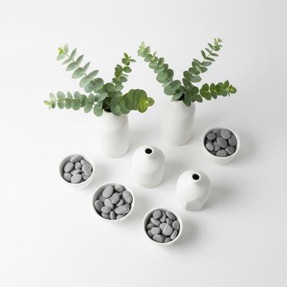 Top-down flat lay of white ceramic vases with eucalyptus and pebbles